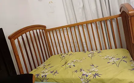 Wooden baby crib with mattress and soft side protective cover.