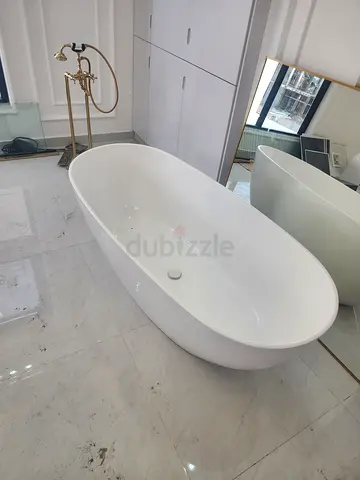 A freestanding oval bathtub in whiteA gold/brass floor-mounted bathtub mixer and hand shower beside
