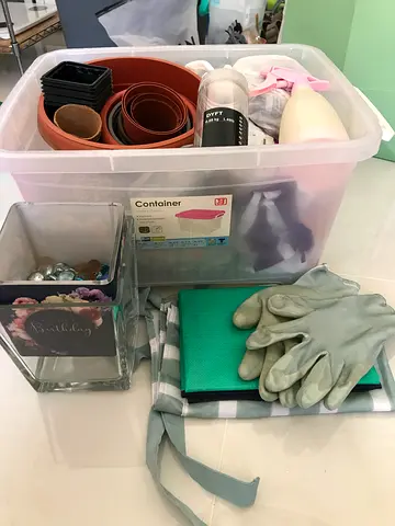 A collection of gardening items and tools stored in a transparent IKEA SAMLA container. The IKEA SAM