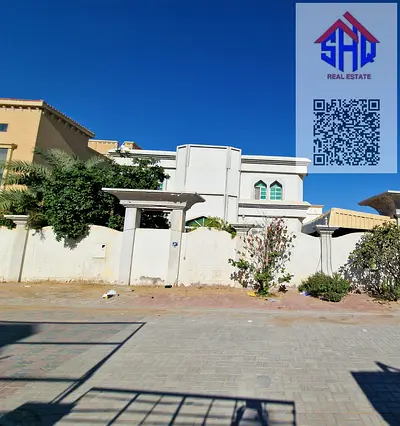 Villa for sale in Al Muwaihat area, near a mosque. Includes water, electricity, and air conditioning. 7 rooms, living room, majlis, and bedroom + storage room.
