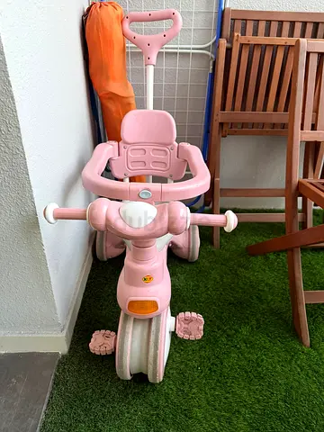Two bikes: pink toddler tricycle with parent push handle and purple pusher