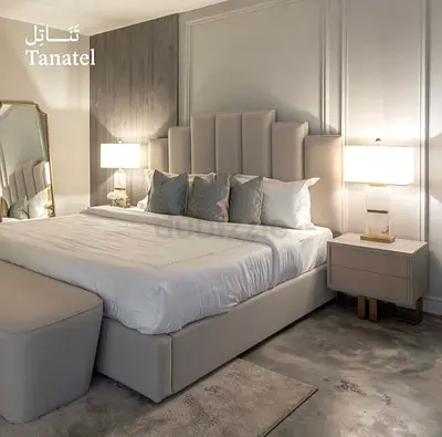 Light grey upholstered bed with tall padded headboard and bedside tables