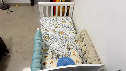 White Crib with Soft Bedding and Nursing Pillow