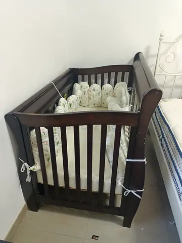 Dark wood sleigh-style baby crib with mattress and bumper