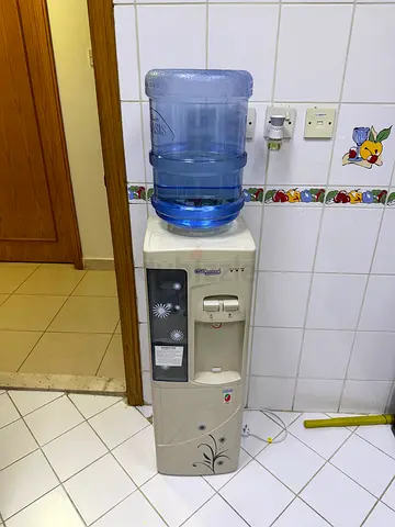Freestanding water dispenser with hot  cold taps and storage cabinet.