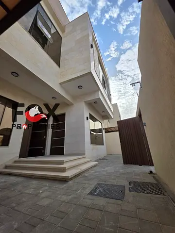 A luxurious villa is for sale in Al Zahiyah, close to all amenities. It boasts deluxe finishing, five master bedrooms, a large living room, a majlis (