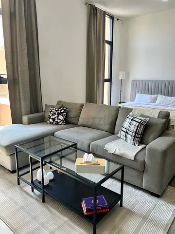 Light grey L-shaped fabric sofa with cushions and glass coffee tables and rug.