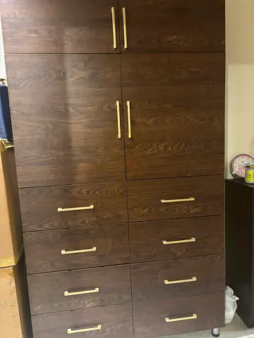 Tall wooden wardrobe with multiple drawers and brass handles