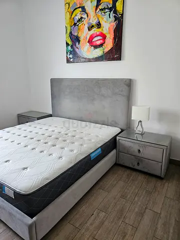 Grey upholstered queen bed frame with mattress and matching nightstands