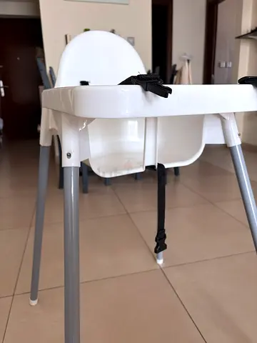 Simple white baby high chair with safety straps.