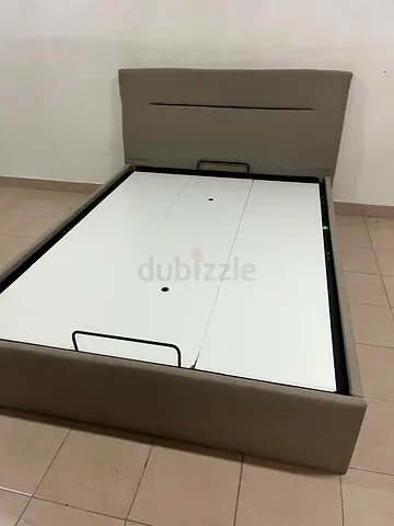 Beige upholstered bed with a hydraulic storage mechanism for raising the mattress.