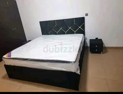 Black upholstered double bed with mattress and bedside table