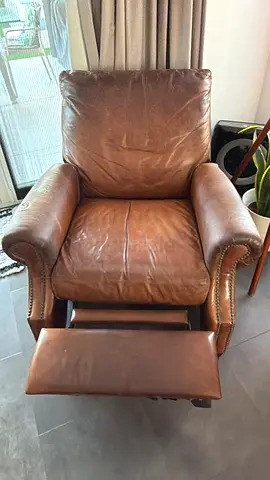 Well-used brown leather reclining armchair with footrest with 2 holes on arm