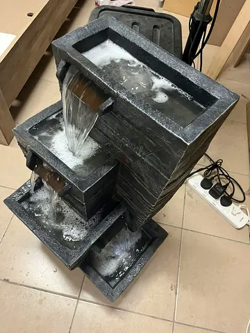 A fountain with a four-tiered cascading waterfall design, made of durable and lightweight resin in a