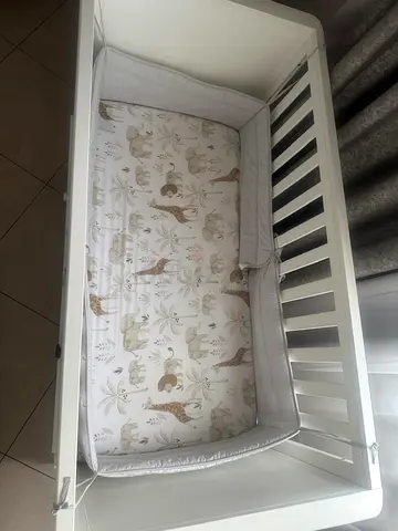 White wooden baby crib with padded bumper and safari-themed mattress