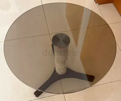Round glass side table with stone center column and wooden tripod base with sofa chair
