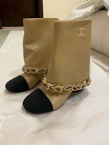 beige leather Chanel ankle boots featuring a black round toe cap and a gold-tone chain detail