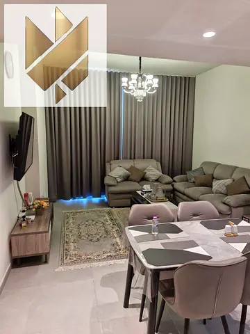 Furnished two-bedroom apartment with a living room for annual rent in Aljada, Sharjah, featuring a gym, swimming pool, parking, and a garden.