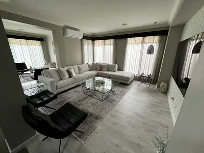 Beautiful beige sectional sofa with modern glass coffee table, side tables and carpet.