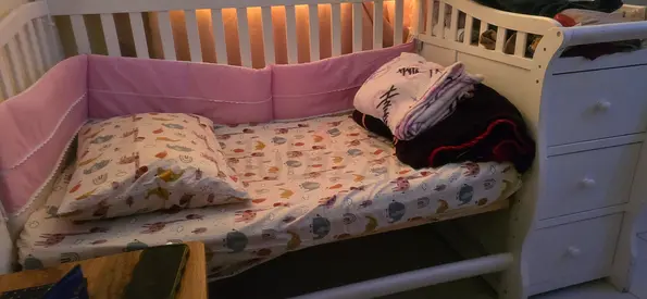 White wooden baby crib with attached changing drawers and bedding included