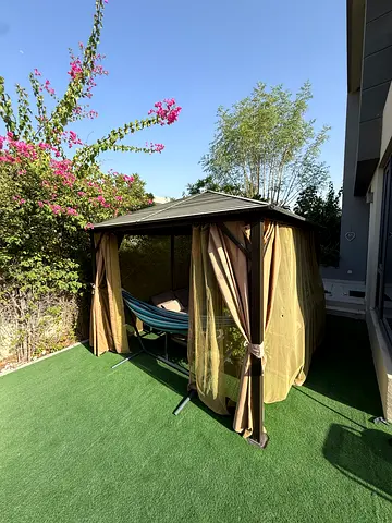 Outdoor gazebo with curtains and hammock on artificial grass.