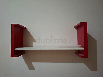 Wall-mounted floating shelf with red brackets in excellent condition