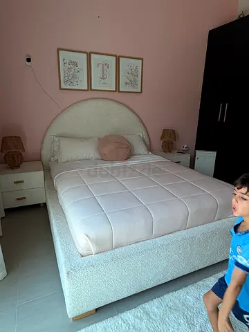 Queen bed with round headboard light beige with mattress and 2 bedside tables and 2 lamps and carpet