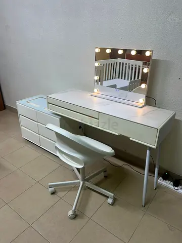 A modern white vanity table with an LED mirror, wireless charger, Bluetooth speaker, and matching ch