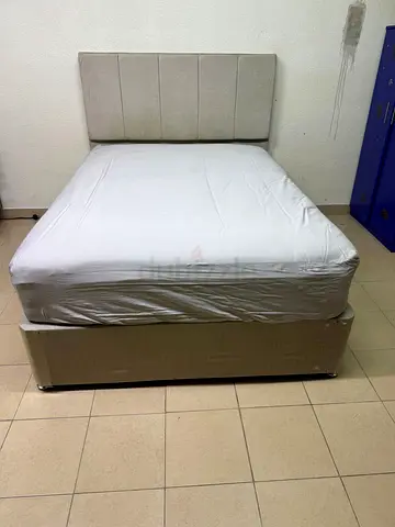 A light beige upholstered bed with a long, padded headboard.