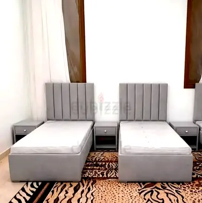 Pair of grey single beds with mattresses and matching bedside tables