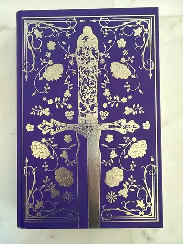 Hardcover Book of Powerless by Lauren Roberts with Decorative Purple Cover and Silver Sword Motif