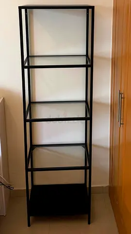 Tall black metal shelving unit with glass shelves
