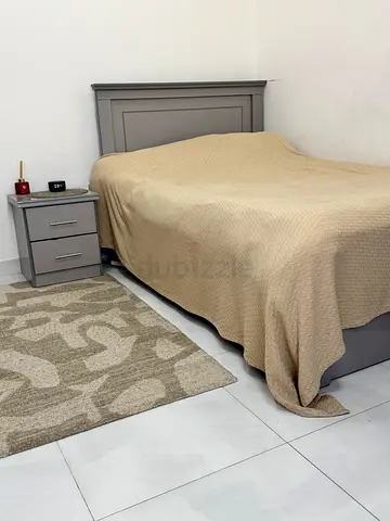 Gray wooden bed frame with matching bedside table and neutral rug