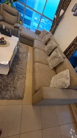 Beige L-shaped sofa with reclining chair and shaggy rug - good condition