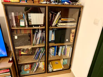 Wooden glass-front bookshelf with multiple books and storage