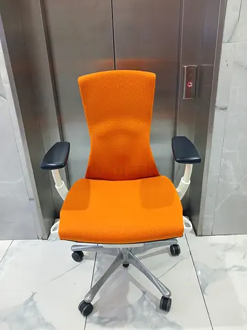 Orange ergonomic Herman Miller Embody office chair with adjustable armrests and swivel base