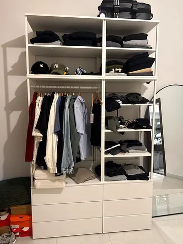 IKEA PAX-style open wardrobe with shelves and drawers, filled with clothes
