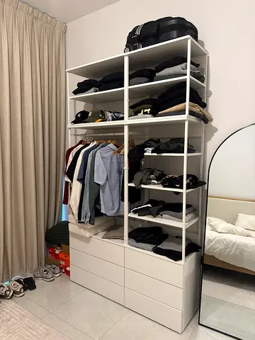 IKEA PAX-style open wardrobe with shelves and drawers, filled with clothes