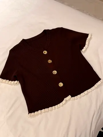 Brown knit short-sleeve top with decorative gold buttons and white ruffle trim