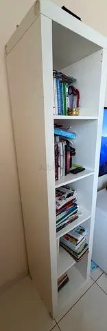 Tall white bookshelf with assorted books and stationery