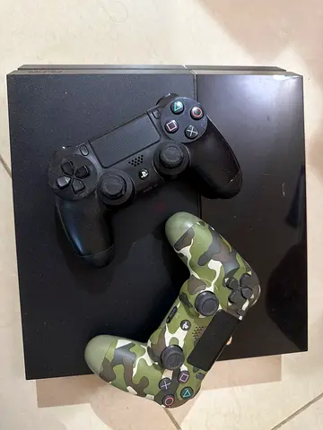 PlayStation 4 console with two DualShock 4 controllers (one camo) and PlayStation Steering Wheel