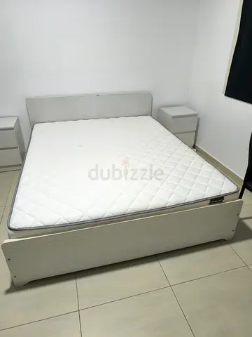 White wooden double bed frame with mattress and two bedside tables