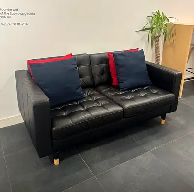 Black tufted two-seater leatherette sofa with wooden legs