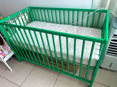 Green wooden baby crib (solid, unused) with mattress
