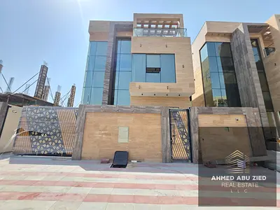 Villa for sale in Ajman, Al Helio 2 area. It consists of a ground floor, first floor, and roof, featuring 6 master bedrooms, a maid's room, two kitche