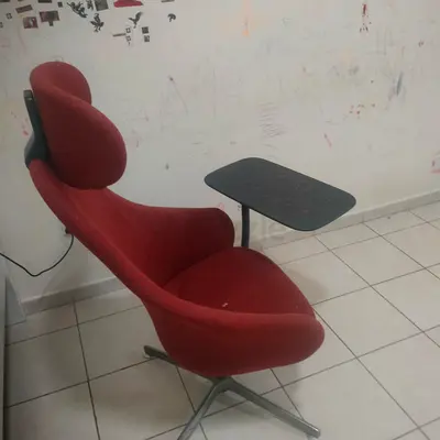 Red swivel lounge chair with attached tablet/side table useful for work from home.