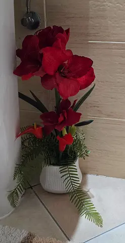 Red artificial amaryllis arrangement in white ceramic pot