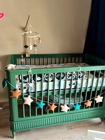 Green wooden baby crib with bumper and decorations. Playen and other baby interactive toys.