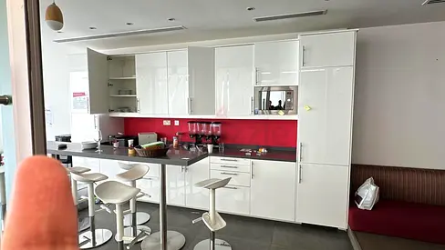Modern white high-gloss fitted kitchen with island and stools.