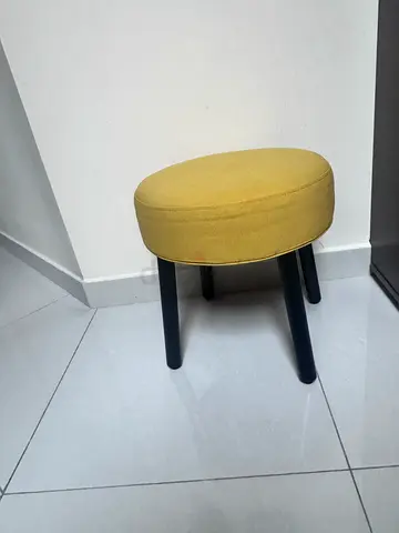 Small round yellow upholstered stool with black legs